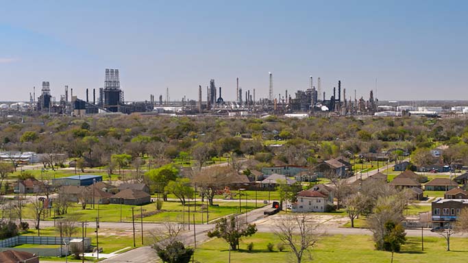 Aerial shot of residential neighborhood with a massive complex of oil refineries in the distance.