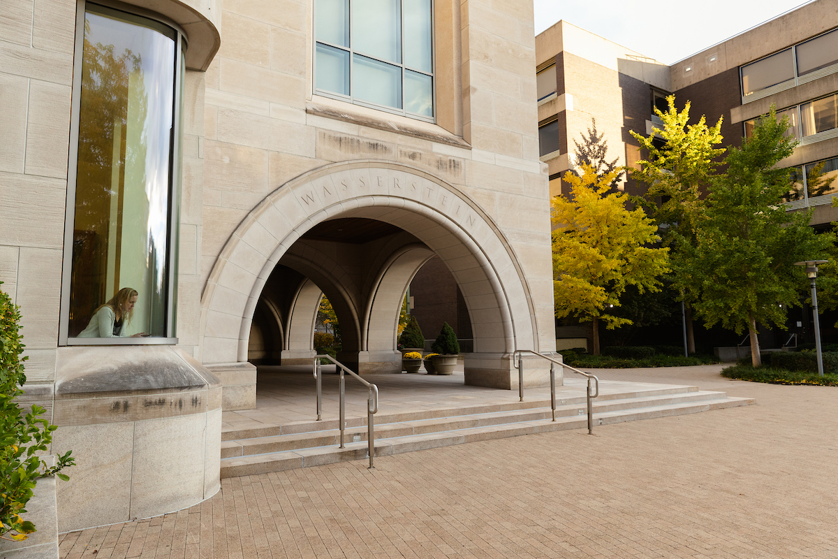 Large stone campus building next to an older concrete and brick building. Trees with changing leaves between the buildings.