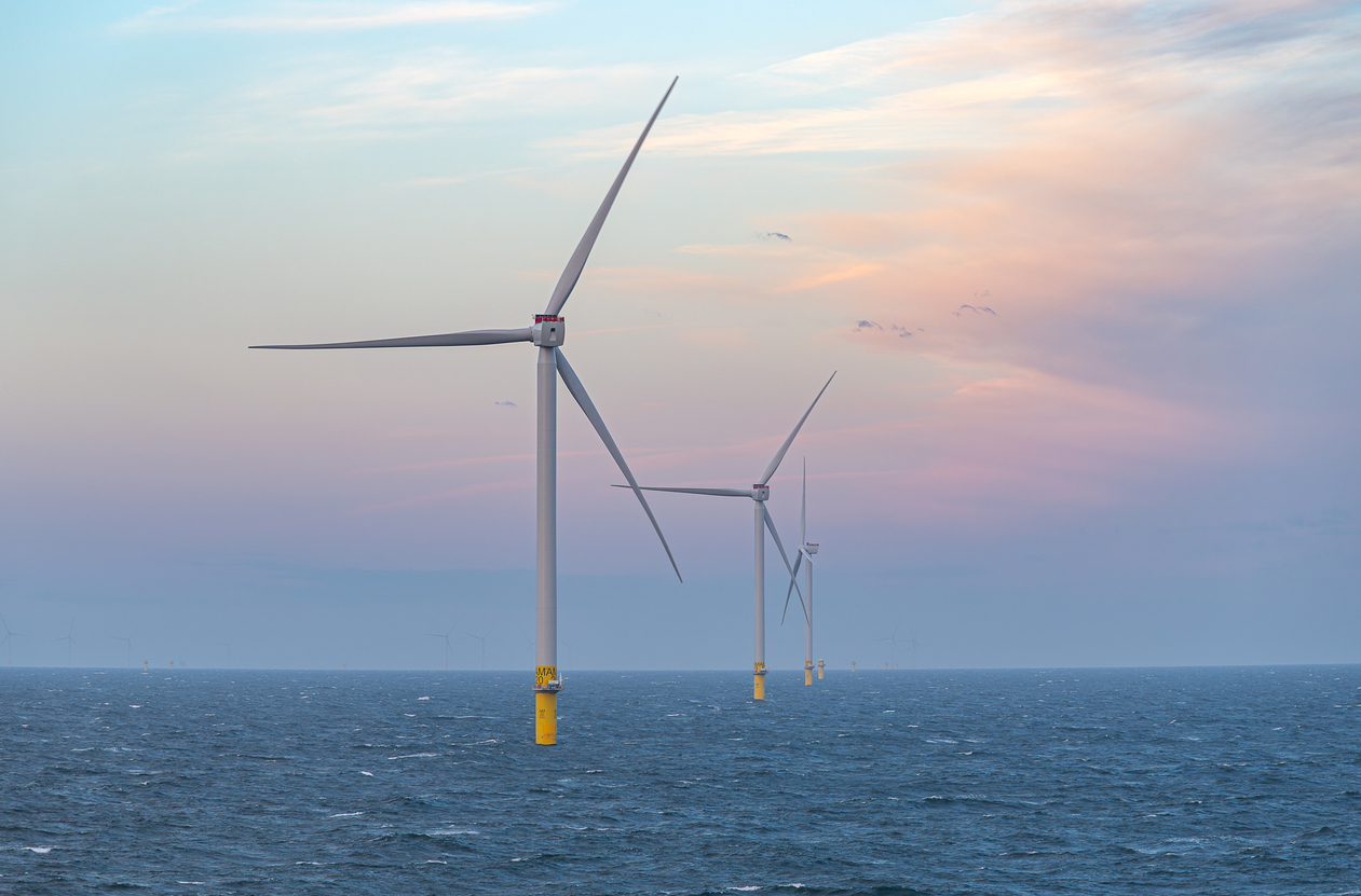Dawn light and pink skies behind a line of offshore wind turbines.